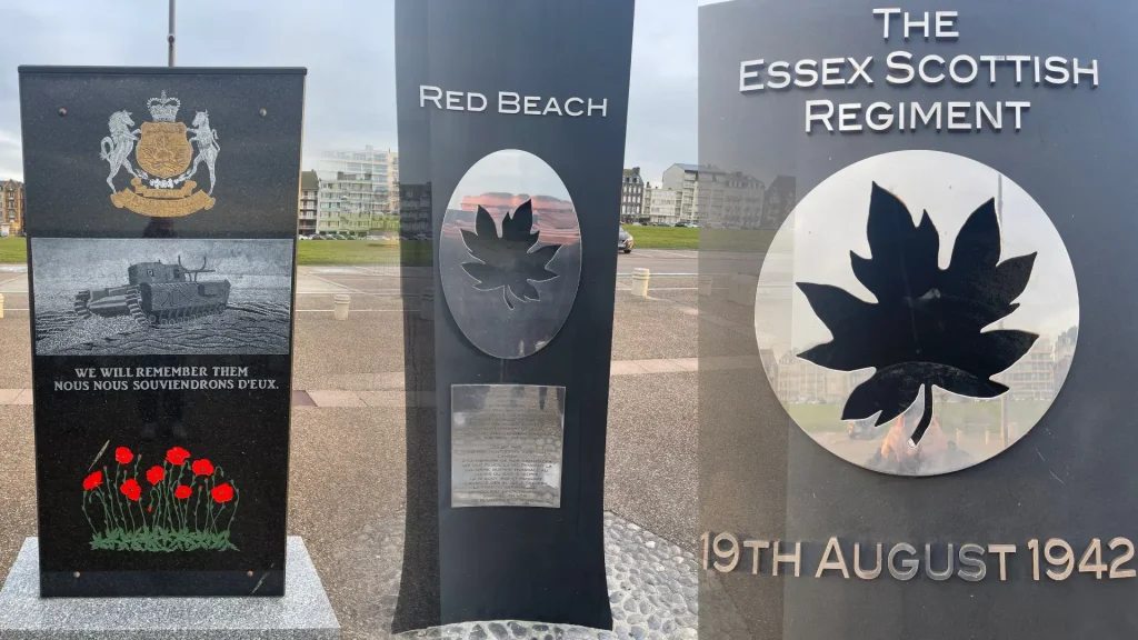 Three commemorative plaques for the essex scottish regiment featuring crests and text, set against a backdrop of a cloudy sky and buildings, with red poppies at the base.
