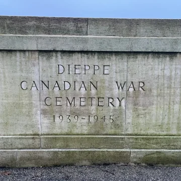 Alt text: a weathered stone plaque at the entrance of the dieppe canadian war cemetery, inscribed with 