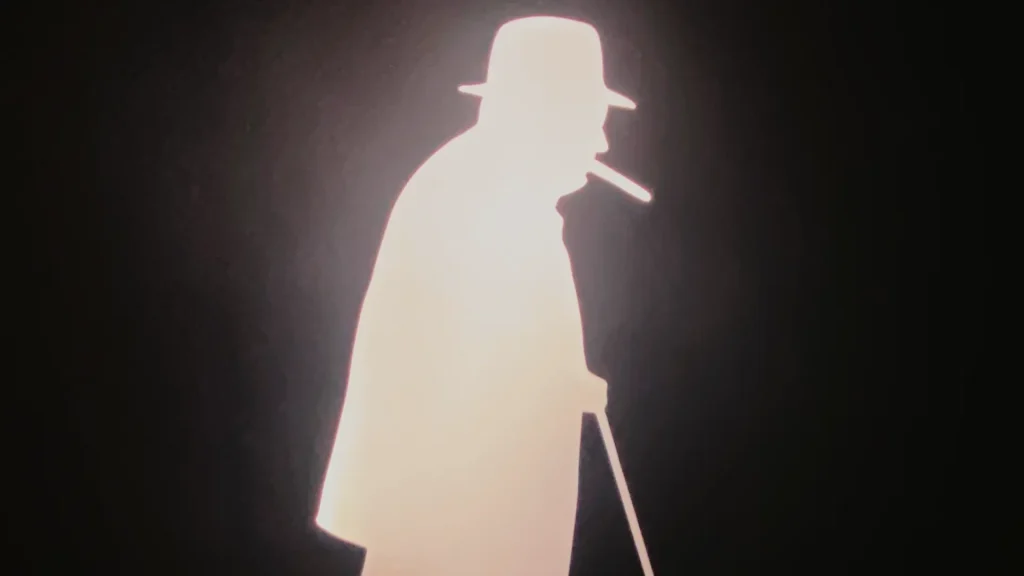 Silhouette of a person in a hat and trench coat, holding a cane, highlighted against a bright light in a dark background. the figure is reminiscent of a classic detective or noir film character.