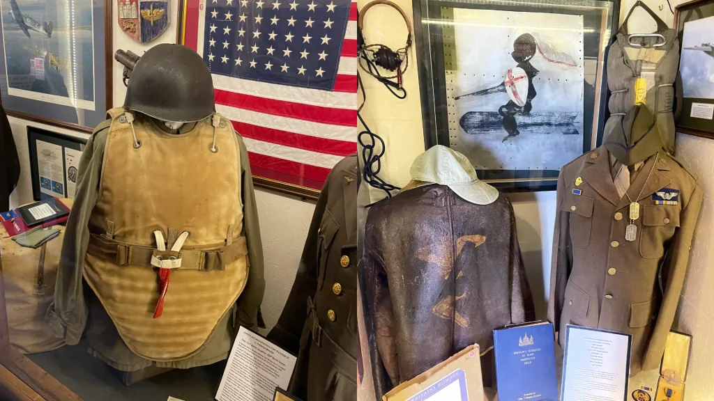 A display of military memorabilia including uniforms, helmets, an american flag, and photos in a museum setting, capturing historical artifacts from various military eras.