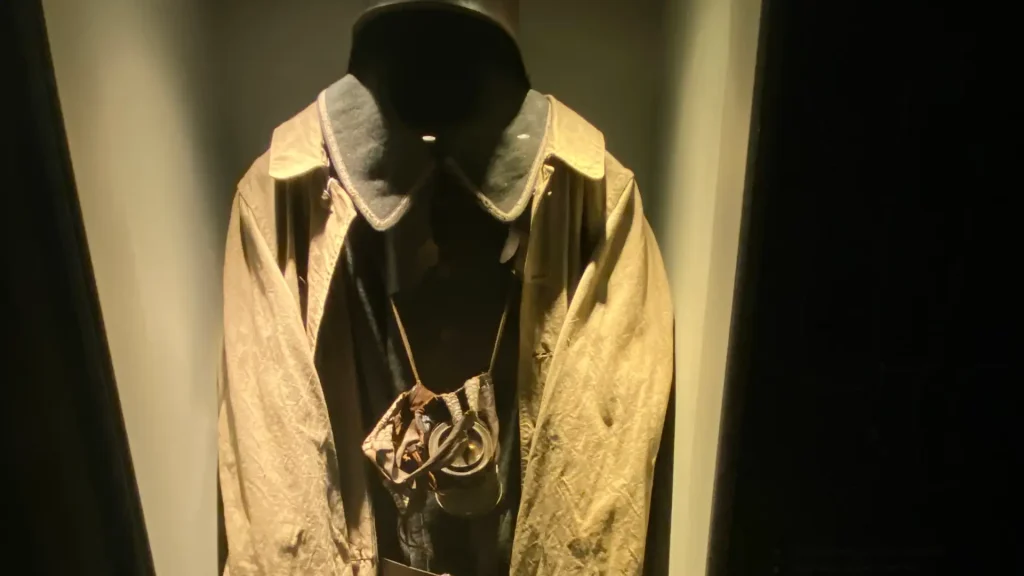 An illuminated display of a vintage golden jacket with a high collar, accessorized with a chain and pendant, set against a dark background.