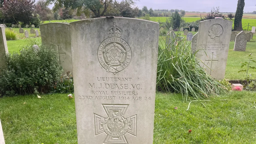 A gravestone of lieutenant m.j. dease, v.c., royal fusiliers, who died on 23rd august 1914 at age 24, with surrounding greenery and other tombstones in the background.