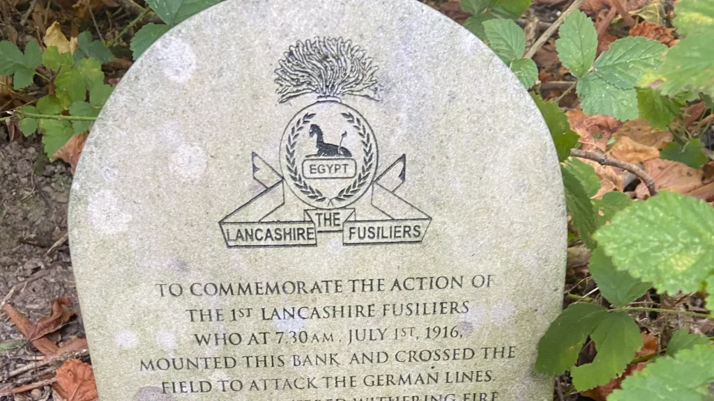 A stone memorial with an engraved emblem commemorating the 1st lancashire fusiliers' action in egypt on july 1st, 1916, surrounded by green foliage.