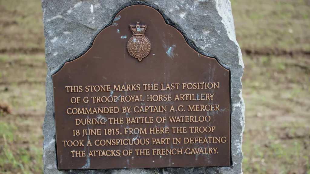 A bronze plaque on a stone marker commemorating where g troop royal horse artillery, led by captain a.c. mercer, made a significant contribution during the battle of waterloo, defeating french cavalry.