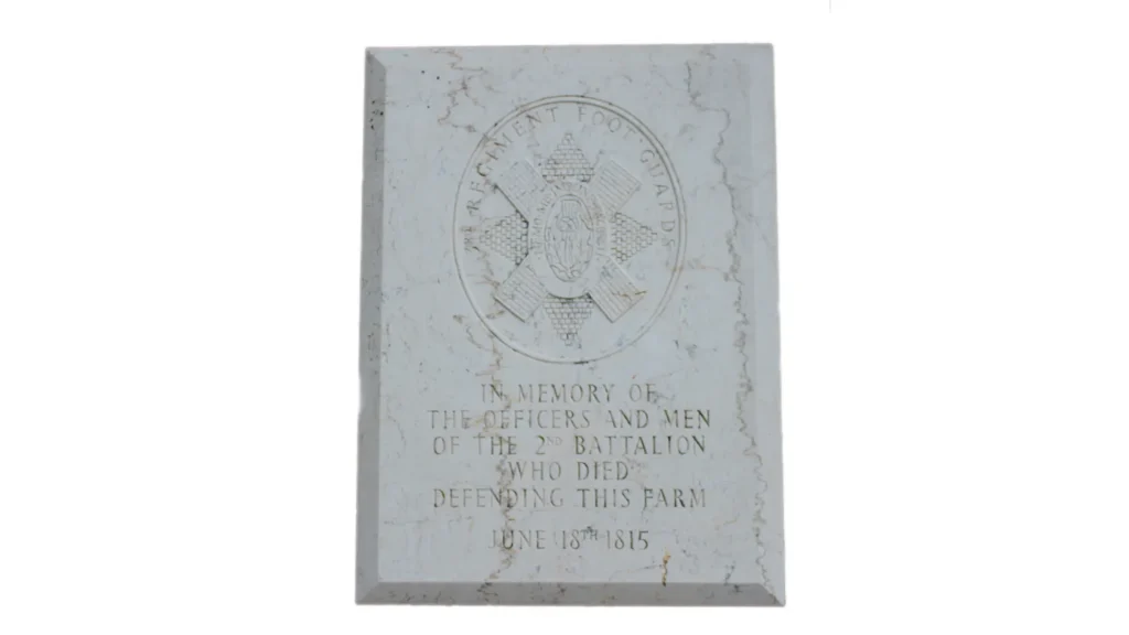 A weathered marble memorial plaque with engraved text and a coat of arms, commemorating the officers and men of the 2nd battalion who died on june 18th, 1815.