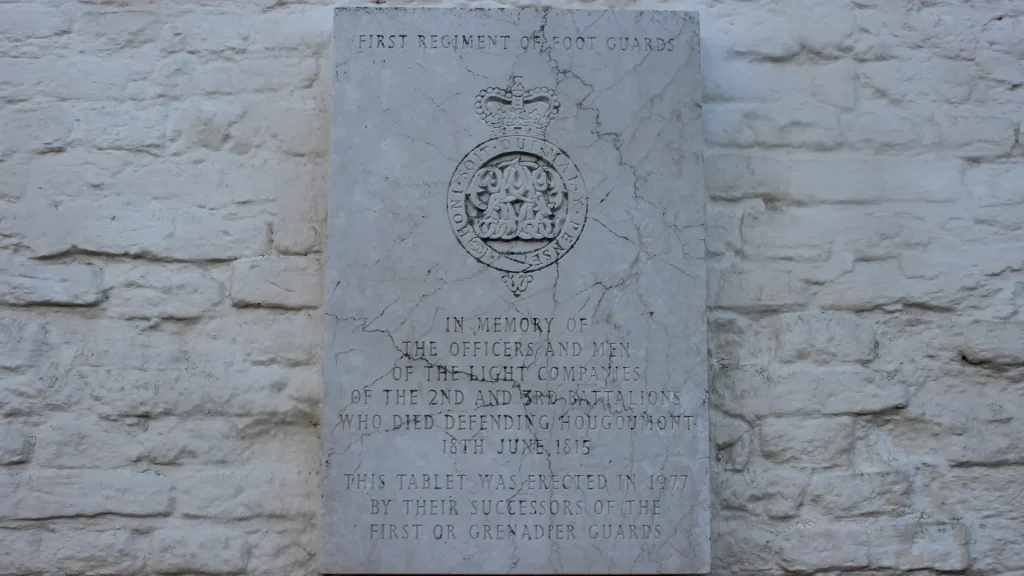 A weathered white memorial stone for the first regiment of foot guards, detailing a dedication to the officers and men who died in 1815, with an inscription indicating it was erected in 1977.
