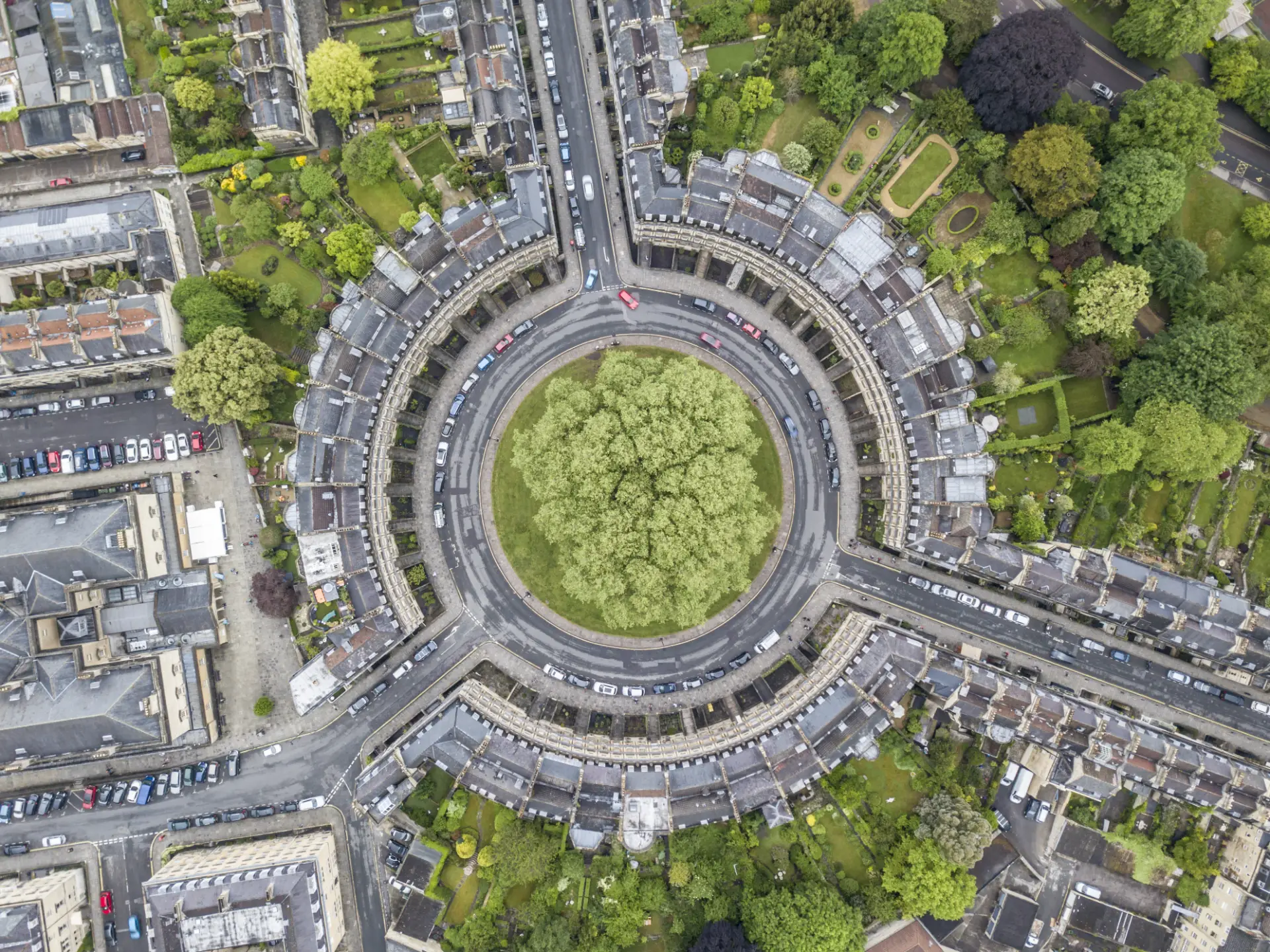 Aerial view of a circular road with cars, surrounded by buildings and greenery, resembling a roundabout, in an urban environment.