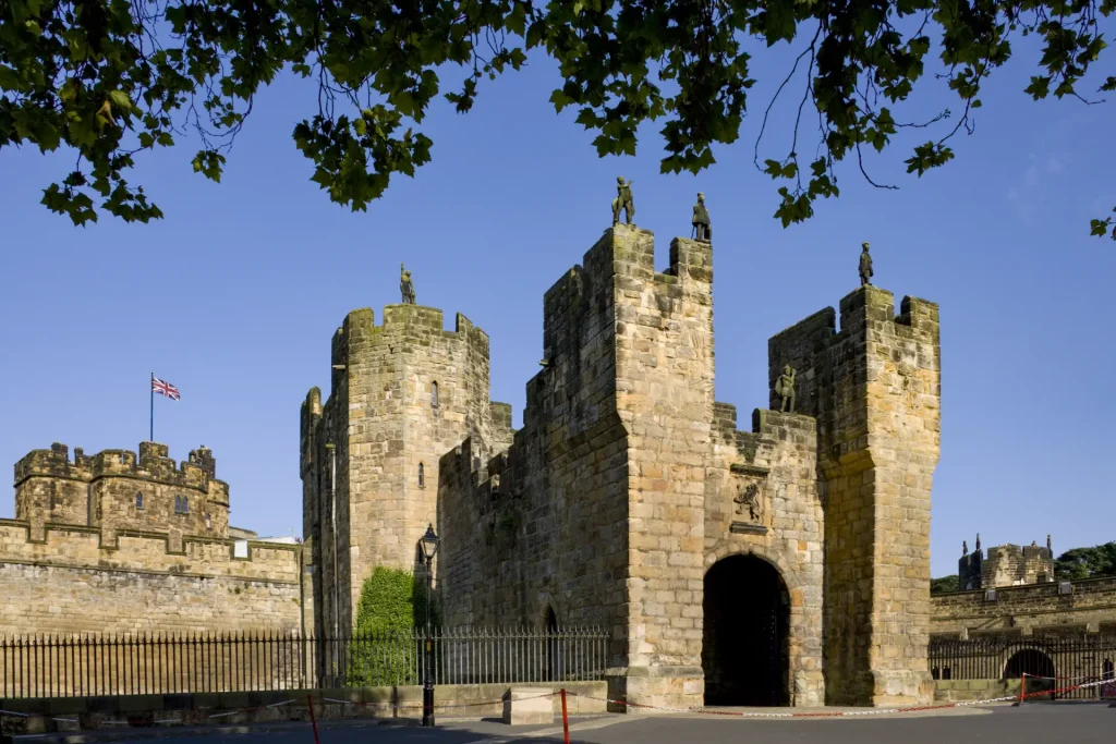 An ancient stone castle with fortified gatehouse, adorned with battlements and flags, under a clear blue sky.