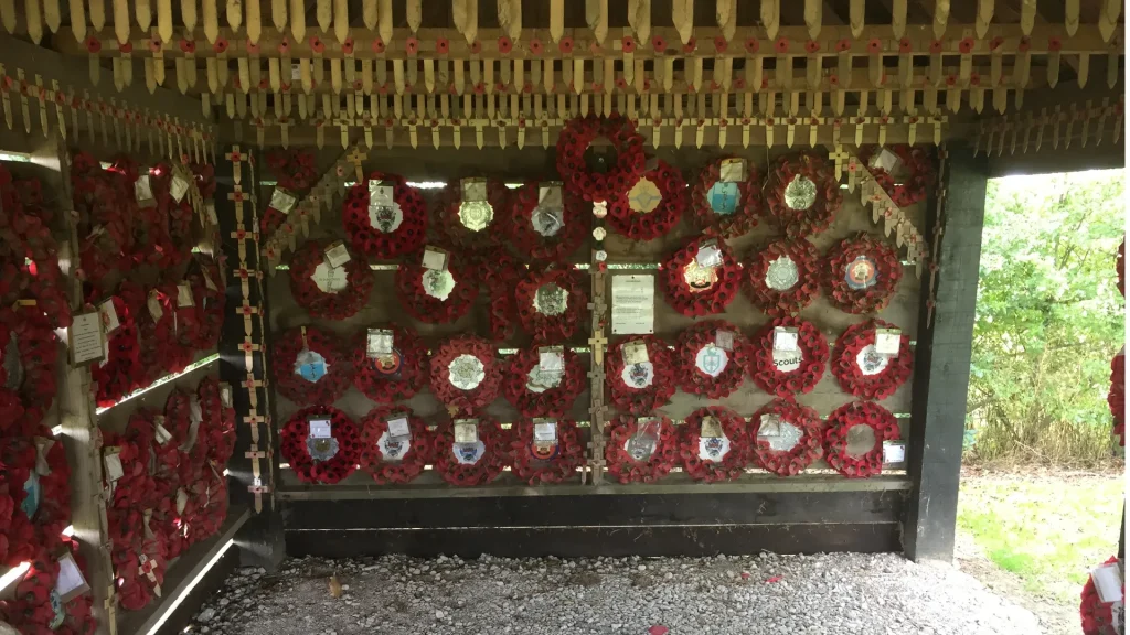 A memorial featuring numerous red poppy wreaths arranged on walls under a shelter, each wreath accompanied by a plaque, creating a poignant tribute space.