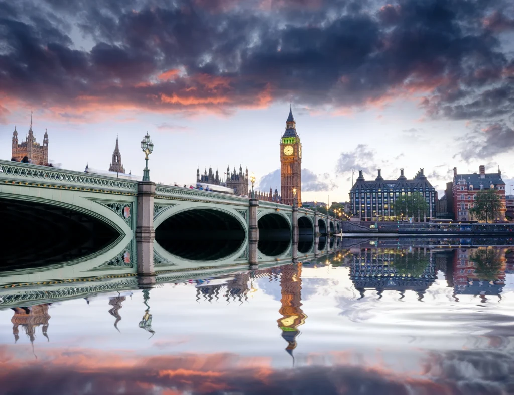 Westminster bridge and the big ben at sunset, with colorful skies and a clear reflection of the landmarks on the river thames in london.