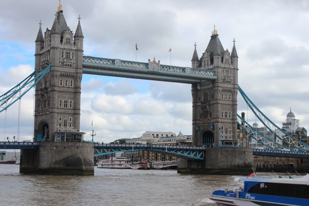 The tower bridge in london, featuring its two iconic towers and a double bascule bridge span, under a cloudy sky.