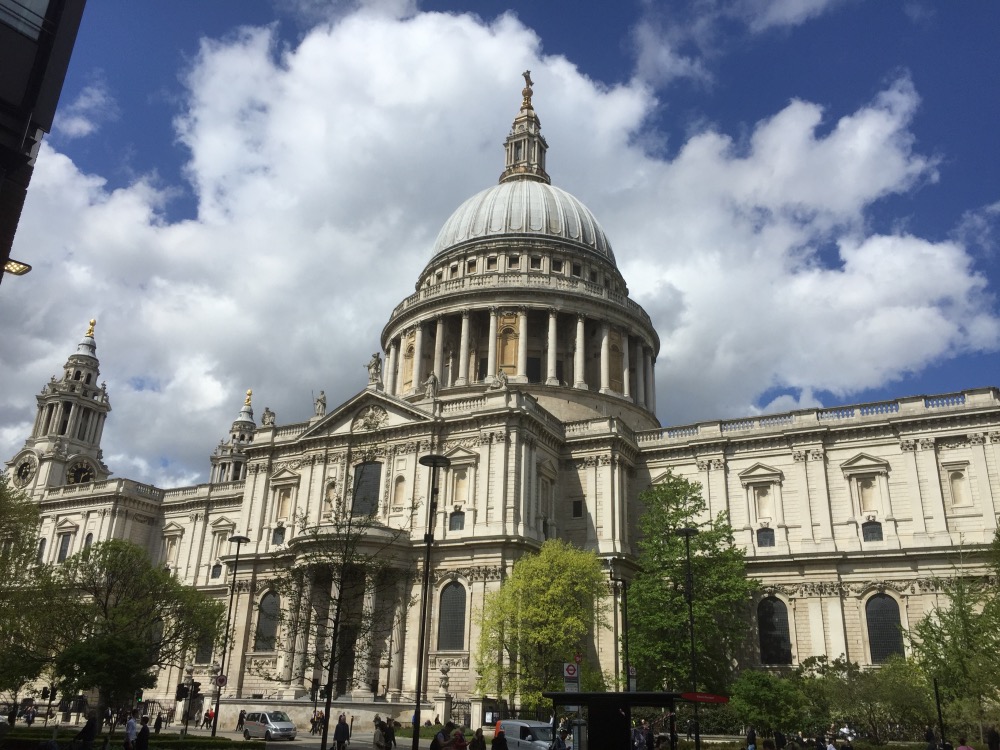A grand view of st. paul's cathedral in london under a partly cloudy sky, with trees and pedestrians visible in the foreground.