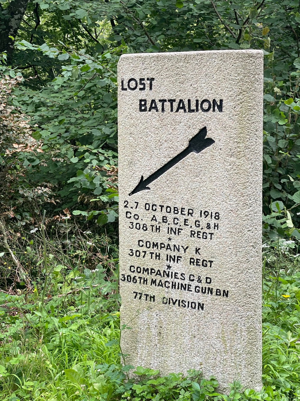 Stone monument in a forested area, inscribed with "lost battalion" and details of military units from october 2-7, 1918, including an arrow symbol.