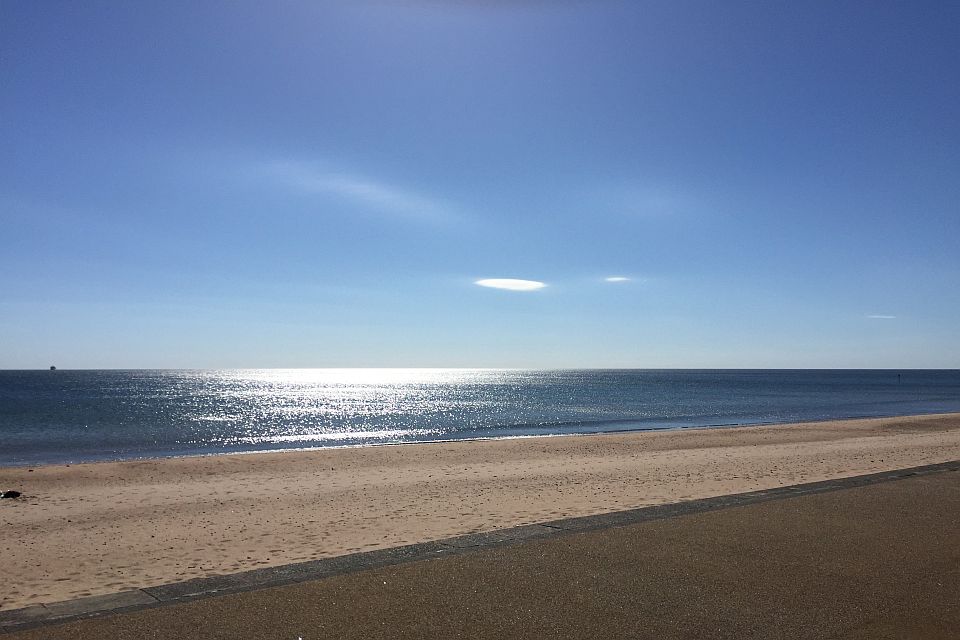 A tranquil beach scene with golden sands, a calm sea reflecting sunlight, and a clear blue sky.