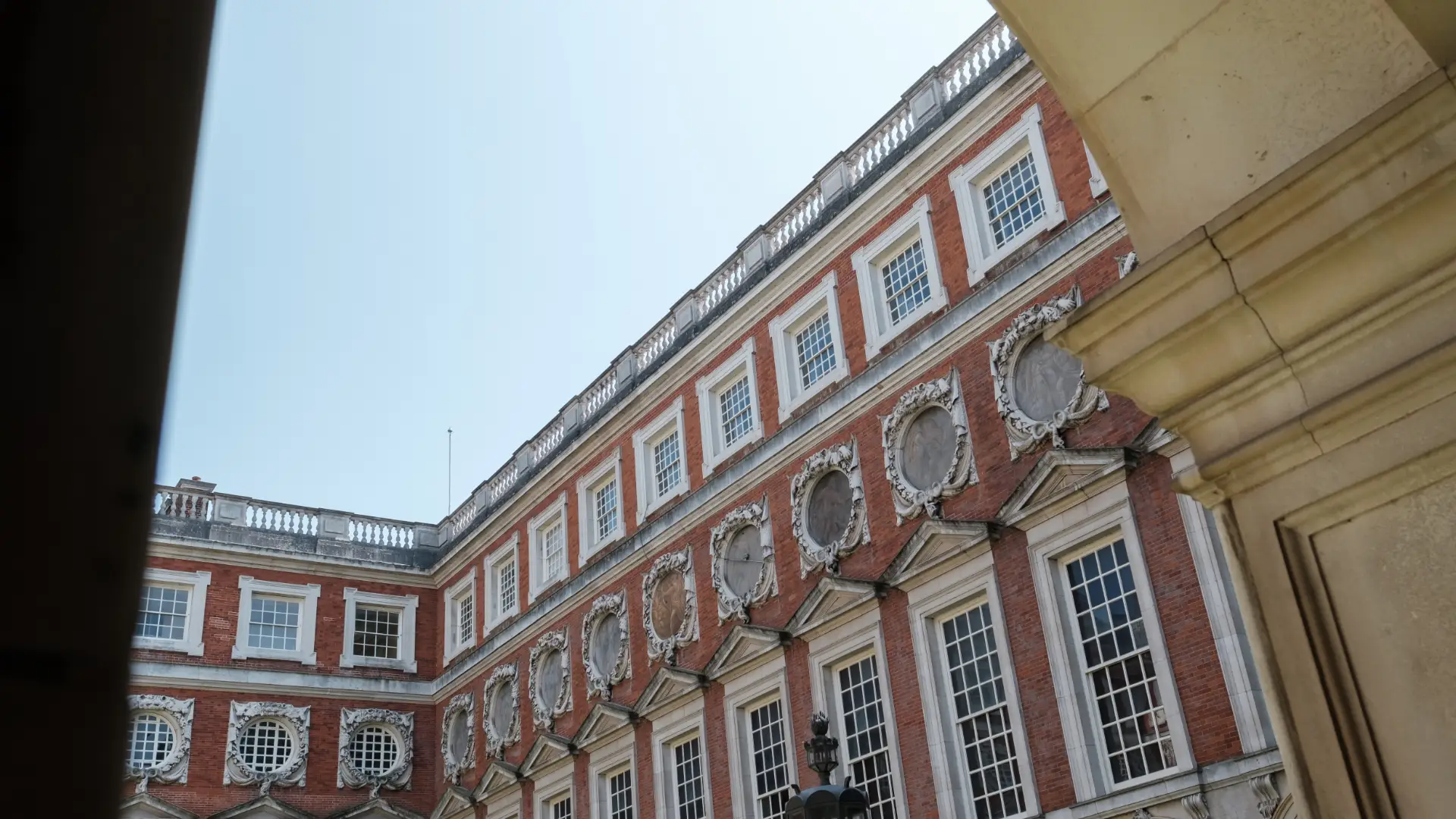 View of an ornate classical building with red and white facade, decorative round windows, under a clear blue sky, partially obscured by a beige architectural column on the left.