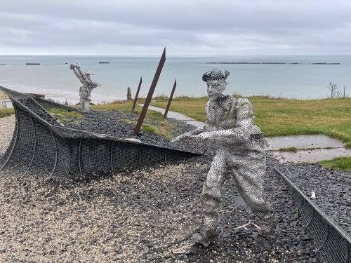 Metal sculptures of a sailor and a fisherman working on nets, with a cloudy sky and ocean in the background, placed in a seaside park.